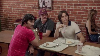 Movie still from “Everybody Wants Some!!” (2016), directed by Richard Linklater – A group of men sitting at a table with plates of food; Medium shot, Over the shoulder angle