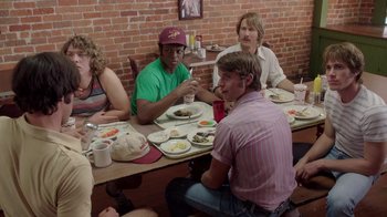 Movie still from “Everybody Wants Some!!” (2016), directed by Richard Linklater – A group of people sitting at a table eating food; Medium shot, Over the shoulder angle