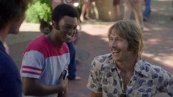 Movie still from “Everybody Wants Some!!” (2016), directed by Richard Linklater – Two young men laughing together on a brick path; Medium shot, Over the shoulder angle