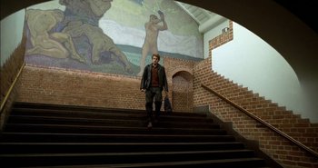 Movie still from “Evil” (2003), directed by Mikael Håfström – A man standing on some steps in front of a mural; Wide shot, Low angle
