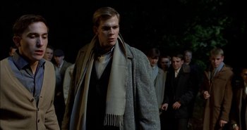 Movie still from “Evil” (2003), directed by Mikael Håfström – A man wearing a coat and a scarf walking down a street; Medium shot, Low angle