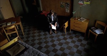 Movie still from “Evil” (2003), directed by Mikael Håfström – A man sitting on the floor of a room reading a piece of paper; Wide shot, High angle