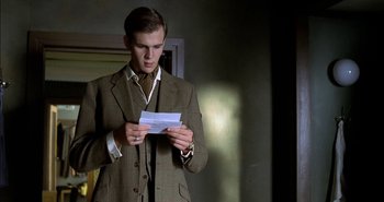 Movie still from “Evil” (2003), directed by Mikael Håfström – A man in a suit and tie looking at a piece of paper; Medium shot, Low angle