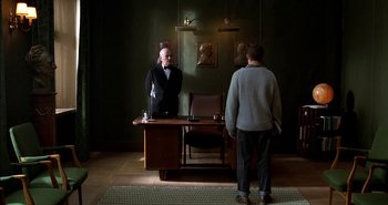 Movie still from “Evil” (2003), directed by Mikael Håfström – A man standing in front of a desk in a room; Wide shot, Over the shoulder angle
