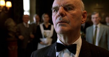 Movie still from “Evil” (2003), directed by Mikael Håfström – An older man wearing a suit and a bow tie; Close Up shot, Low angle