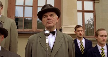 Movie still from “Evil” (2003), directed by Mikael Håfström – An older man wearing a suit and a hat; Medium shot, Low angle