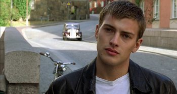 Movie still from “Evil” (2003), directed by Mikael Håfström – A young man standing on the side of the street; Close Up shot, Over the shoulder angle