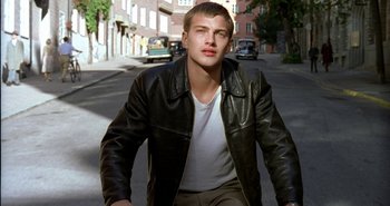 Movie still from “Evil” (2003), directed by Mikael Håfström – A man in a black leather jacket riding a bike down a street; Medium shot, Over the shoulder angle
