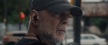 Movie still from “Glass” (2019), directed by M. Night Shyamalan – An older man wearing a baseball cap and ear buds; Close Up shot, Low angle