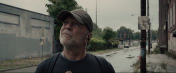 Movie still from “Glass” (2019), directed by M. Night Shyamalan – An older man wearing a hat and ear buds looking up; Close Up shot, Low angle