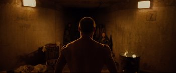 Movie still from “Glass” (2019), directed by M. Night Shyamalan – A man standing in front of a group of people in a dark room; Wide shot, Over the shoulder angle