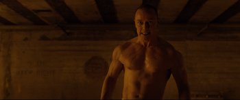 Movie still from “Glass” (2019), directed by M. Night Shyamalan – A man with a muscular body standing in a room; Medium shot, Low angle
