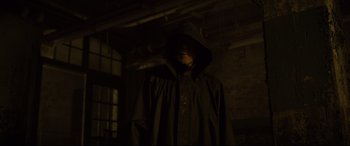 Movie still from “Glass” (2019), directed by M. Night Shyamalan – A man in a black raincoat standing in a dark room; Medium shot, Over the shoulder angle