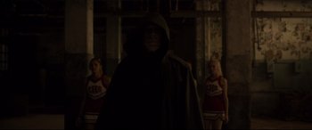 Movie still from “Glass” (2019), directed by M. Night Shyamalan – A man in a hooded cloak standing in front of a group of cheerleaders; Medium shot, Low angle