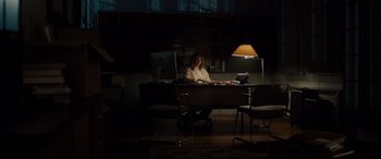 Movie still from “Glass” (2019), directed by M. Night Shyamalan – A woman sitting at a desk in a dark room; Wide shot, High angle