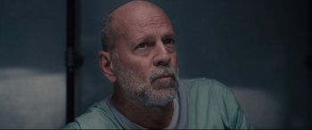 Movie still from “Glass” (2019), directed by M. Night Shyamalan – An older man with a gray beard looking to his left; Close Up shot, Low angle