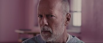 Movie still from “Glass” (2019), directed by M. Night Shyamalan – An older man with a shaved head and a beard; Close Up shot, Over the shoulder angle