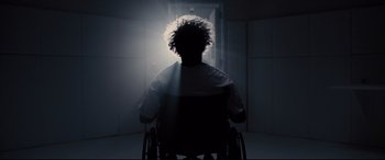 Movie still from “Glass” (2019), directed by M. Night Shyamalan – A person in a wheelchair in a dark room; Medium shot, Low angle