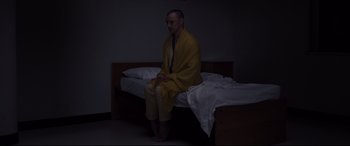 Movie still from “Glass” (2019), directed by M. Night Shyamalan – A man sitting on a bed wearing a yellow robe; Medium shot, High angle