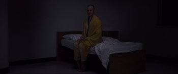 Movie still from “Glass” (2019), directed by M. Night Shyamalan – A man sitting on a bed in a room; Wide shot, High angle