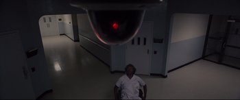 Movie still from “Glass” (2019), directed by M. Night Shyamalan – A man sitting in front of a red light in a room; Wide shot, Overhead angle