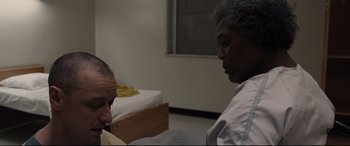 Movie still from “Glass” (2019), directed by M. Night Shyamalan – A man and a woman sitting in front of each other in front of a bed; Close Up shot, Over the shoulder angle