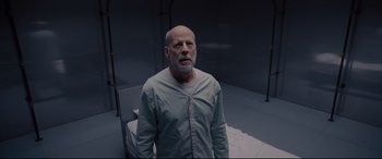 Movie still from “Glass” (2019), directed by M. Night Shyamalan – An older man standing in a room next to a bed; Medium shot, High angle