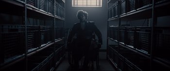 Movie still from “Glass” (2019), directed by M. Night Shyamalan – A man sitting in a chair in a room; Wide shot, Low angle