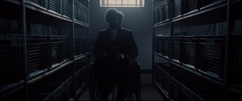 Movie still from “Glass” (2019), directed by M. Night Shyamalan – A man in a suit sitting in a chair in a room; Wide shot, Low angle
