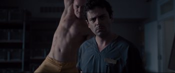 Movie still from “Glass” (2019), directed by M. Night Shyamalan – A man standing next to another man in a dark room; Medium shot, Low angle