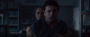 Movie still from “Glass” (2019), directed by M. Night Shyamalan – Two men in a dark room one of them is angry; Medium shot, Over the shoulder angle