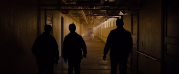 Movie still from “Glass” (2019), directed by M. Night Shyamalan – A group of people walking down a dark hallway; Extreme Wide shot, High angle