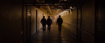 Movie still from “Glass” (2019), directed by M. Night Shyamalan – Three men are walking down a hallway in a building; Wide shot, High angle