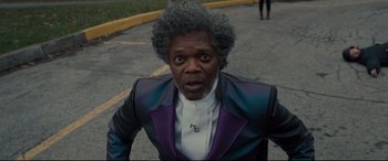 Movie still from “Glass” (2019), directed by M. Night Shyamalan – A man in a purple and black jacket standing in the street; Close Up shot, High angle