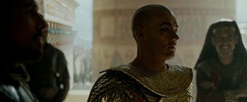 Movie still from “Exodus: Gods and Kings” (2014), directed by Ridley Scott – A bald man in a gold and black costume; Close Up shot, Over the shoulder angle