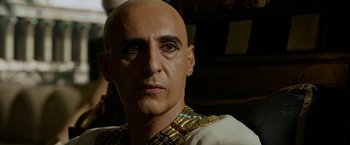 Movie still from “Exodus: Gods and Kings” (2014), directed by Ridley Scott – A bald man wearing a gold and black shirt; Close Up shot, Over the shoulder angle