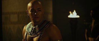 Movie still from “Exodus: Gods and Kings” (2014), directed by Ridley Scott – A bald man wearing a necklace of gold; Close Up shot, Over the shoulder angle