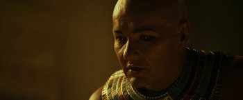 Movie still from “Exodus: Gods and Kings” (2014), directed by Ridley Scott – A man in a gold and black necklace looking to his left; Close Up shot, Over the shoulder angle