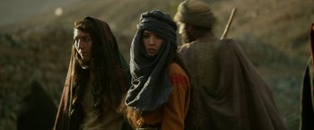 Movie still from “Exodus: Gods and Kings” (2014), directed by Ridley Scott – A woman with a head covering is standing in front of a group of people; Medium shot, Over the shoulder angle