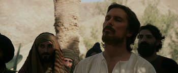 Movie still from “Exodus: Gods and Kings” (2014), directed by Ridley Scott – A man with long hair and a beard standing next to a tree; Close Up shot, Low angle