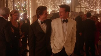 Movie still from “Eyes Wide Shut” (1999), directed by Stanley Kubrick – Two men in tuxedos standing next to each other at an event; Medium shot, Over the shoulder angle