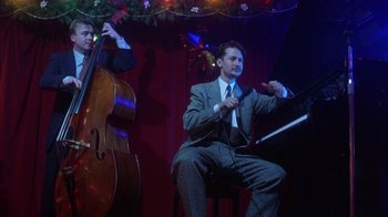 Movie still from “Eyes Wide Shut” (1999), directed by Stanley Kubrick – A man sitting on a chair with a microphone and another man standing next to him; Medium shot, Low angle