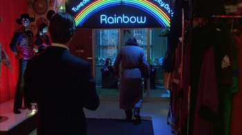 Movie still from “Eyes Wide Shut” (1999), directed by Stanley Kubrick – A woman walking in front of a store with a rainbow sign; Wide shot, Over the shoulder angle
