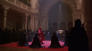 Movie still from “Eyes Wide Shut” (1999), directed by Stanley Kubrick – A group of people dressed in black and red in a room; Extreme Wide shot, High angle