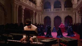 Movie still from “Eyes Wide Shut” (1999), directed by Stanley Kubrick – A man in a white suit playing the piano in front of a group of people; Extreme Wide shot, High angle