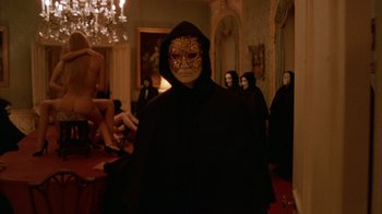 Movie still from “Eyes Wide Shut” (1999), directed by Stanley Kubrick – A person wearing a mask in a room with other people; Wide shot, Low angle