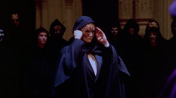 Movie still from “Eyes Wide Shut” (1999), directed by Stanley Kubrick – A man in a black suit and a leopard mask in front of a group of people; Medium shot, High angle