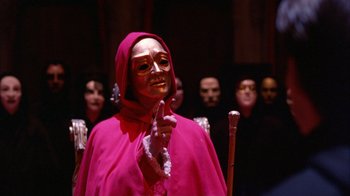 Movie still from “Eyes Wide Shut” (1999), directed by Stanley Kubrick – A woman wearing a mask and holding a cane in front of a group of people; Medium shot, High angle