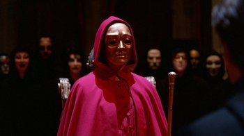 Movie still from “Eyes Wide Shut” (1999), directed by Stanley Kubrick – A woman in a red robe and a gold mask; Close Up shot, Low angle