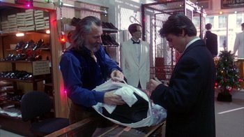 Movie still from “Eyes Wide Shut” (1999), directed by Stanley Kubrick – Two men in tuxedos and a man in a blue shirt; Medium shot, Over the shoulder angle